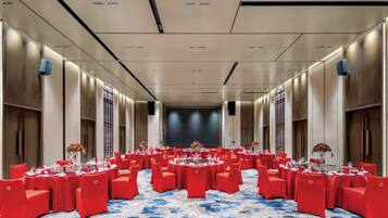 A large conference room with round tables and red chairs, a blue patterned carpet, and a stage at the front.