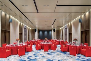 Une grande salle de conférence avec des tables rondes et des chaises rouges, une moquette bleue à motifs et une scène à l’avant.