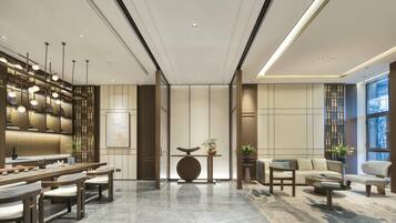 A modern hotel lobby with a central reception desk, seating area, and large windows offering views.