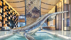 A modern lobby with a large glass sculpture, a patterned wall, and a reception desk. - Voco Xiong An (Baoding)