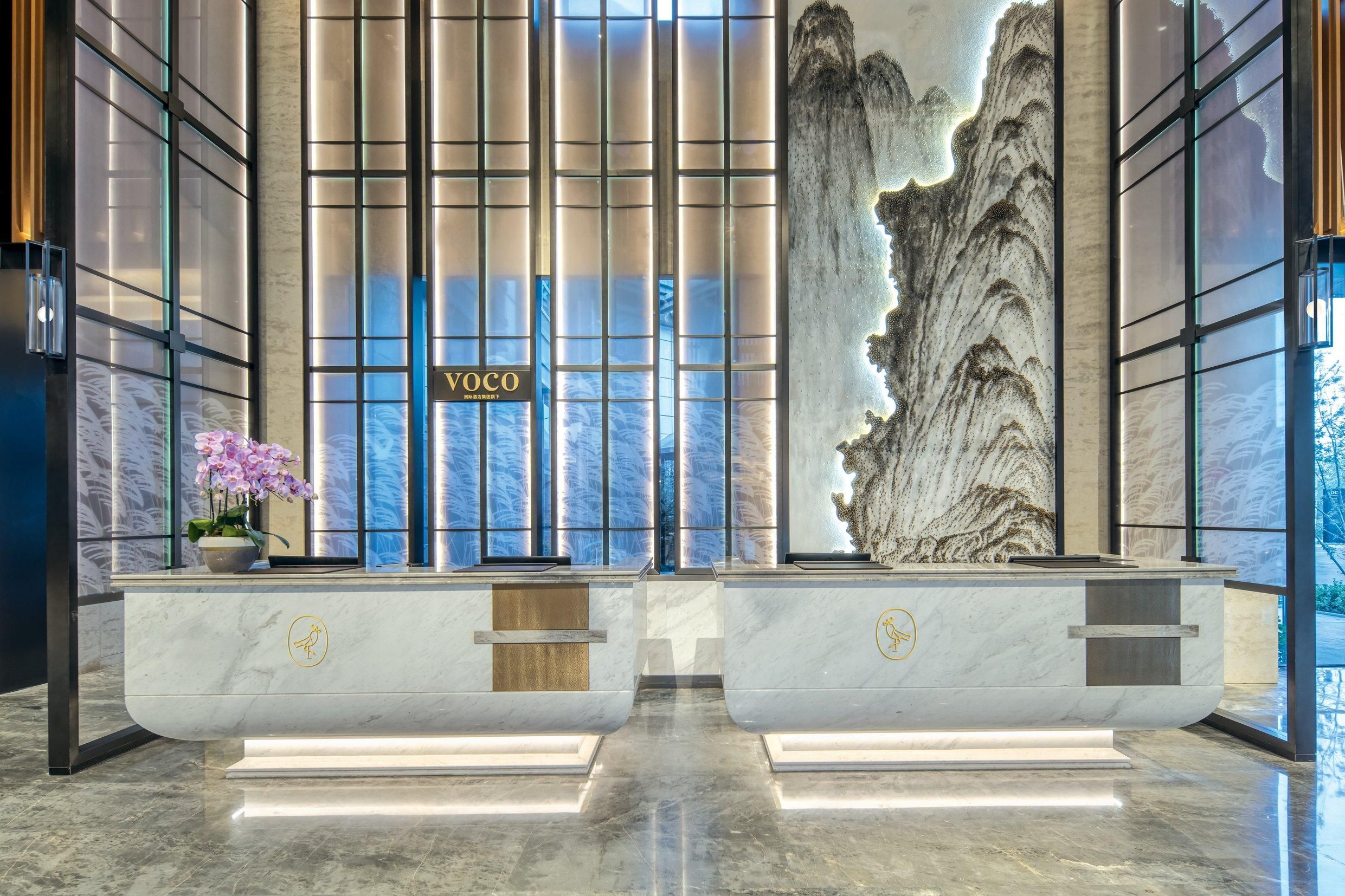 A reception area with a modern design, featuring a large mural, a reception desk, and a potted orchid.