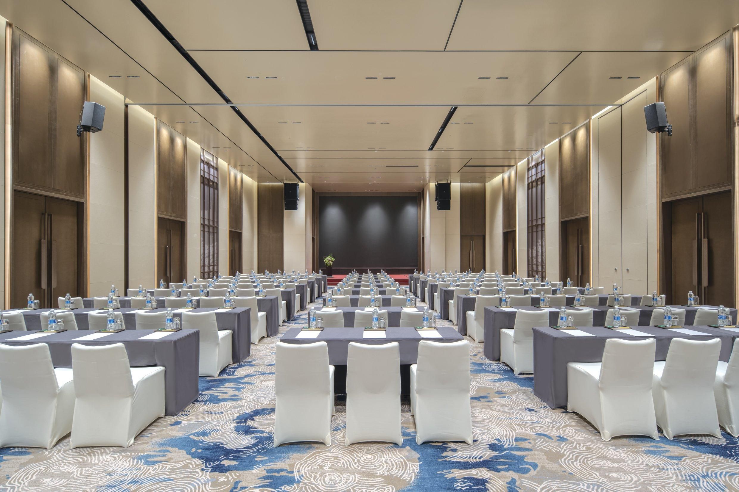 A conference room with rows of tables and chairs, equipped with water bottles and nameplates, and a stage at the front.