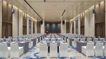 A conference room with rows of tables and chairs, equipped with water bottles and nameplates, and a stage at the front.