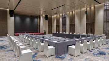A conference room with a long table, white chairs, and a stage.