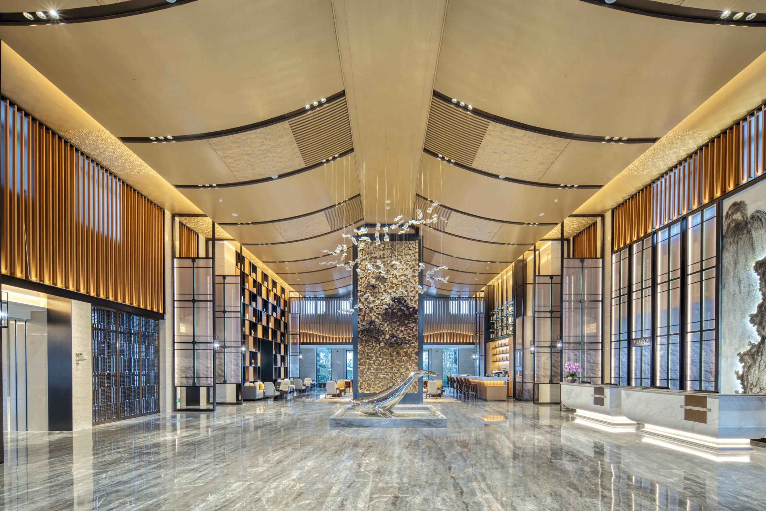 Um hall amplo com uma coluna decorativa central, áreas de estar e um design de teto moderno.