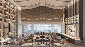 Un salon moderne offrant une vue sur la ville, avec un espace de détente central agrémenté de tables rondes et de canapés, un bar avec des étagères remplies de bouteilles et un plafond décoré de motifs.