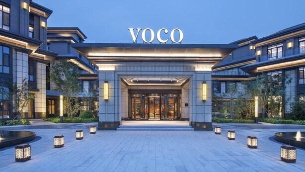 A modern hotel entrance with a prominent "VOCO" sign, a well-lit entrance, and a landscaped area with lanterns. - Voco Xiong An (Baoding)