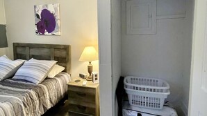 Un dormitorio con cama, mesita de noche, lámpara y un cuadro colgado en la pared.