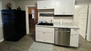Una cocina compacta con armarios blancos, lavavajillas de acero inoxidable y refrigerador negro.