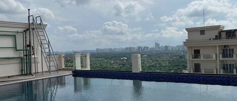 A rooftop swimming pool with a cityscape view, a ladder, and a water filtration system.