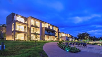 Un edificio moderno de varios pisos con amplias ventanas y un exterior bien iluminado al anochecer.