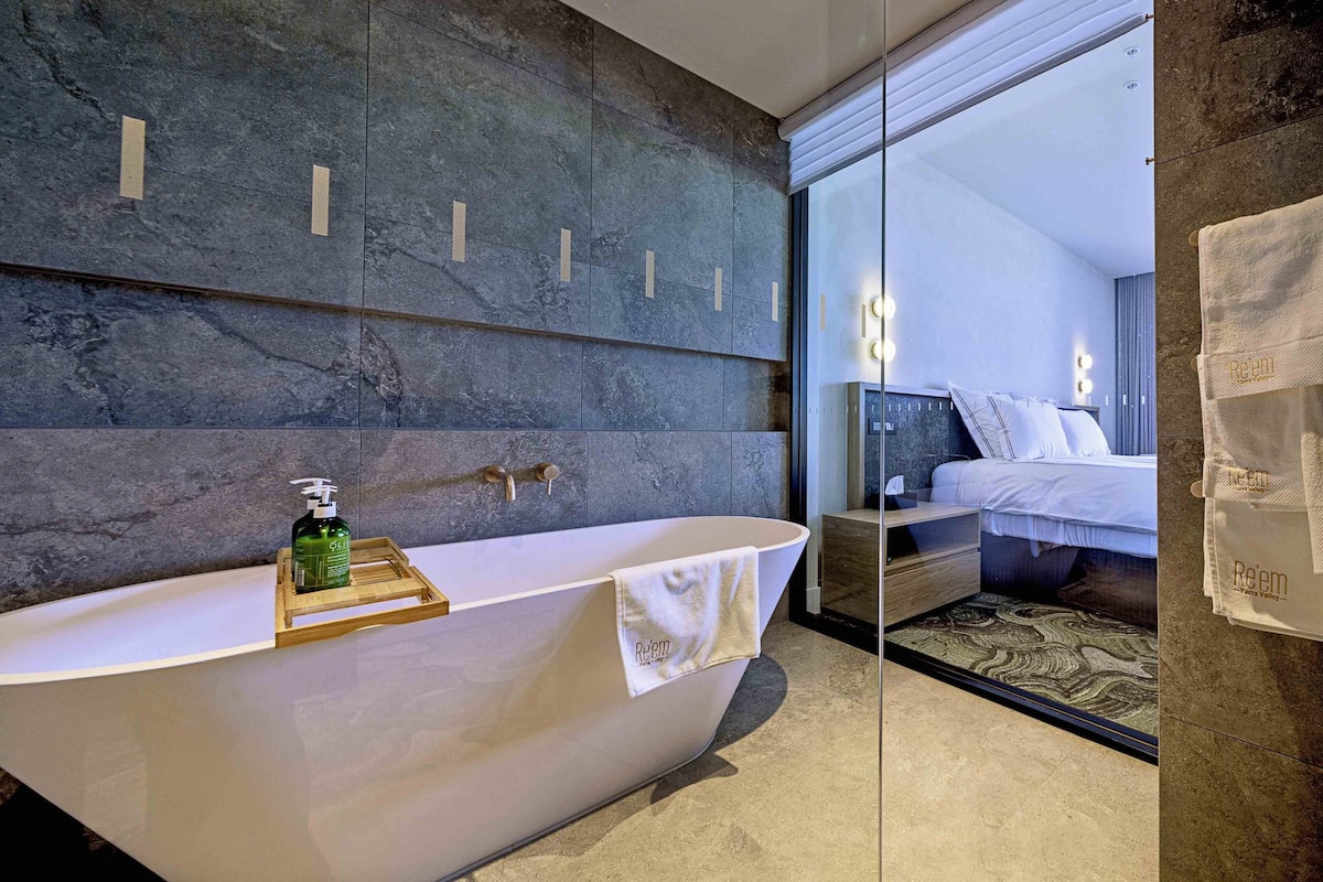 A modern bathroom with a freestanding bathtub, a wooden tray with a bottle, and a towel hanging on the side.