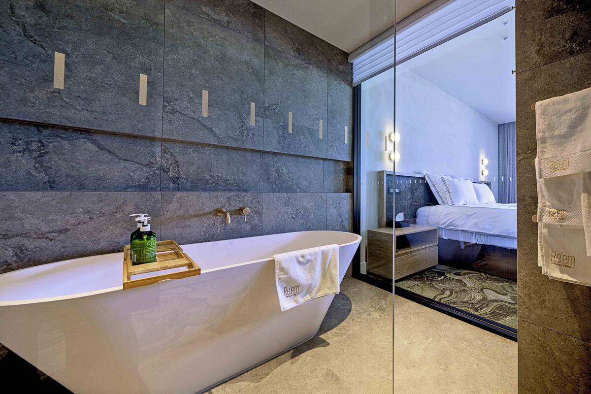 Un baño moderno con una bañera independiente, una bandeja de madera con una botella y una toalla colgada al lado.