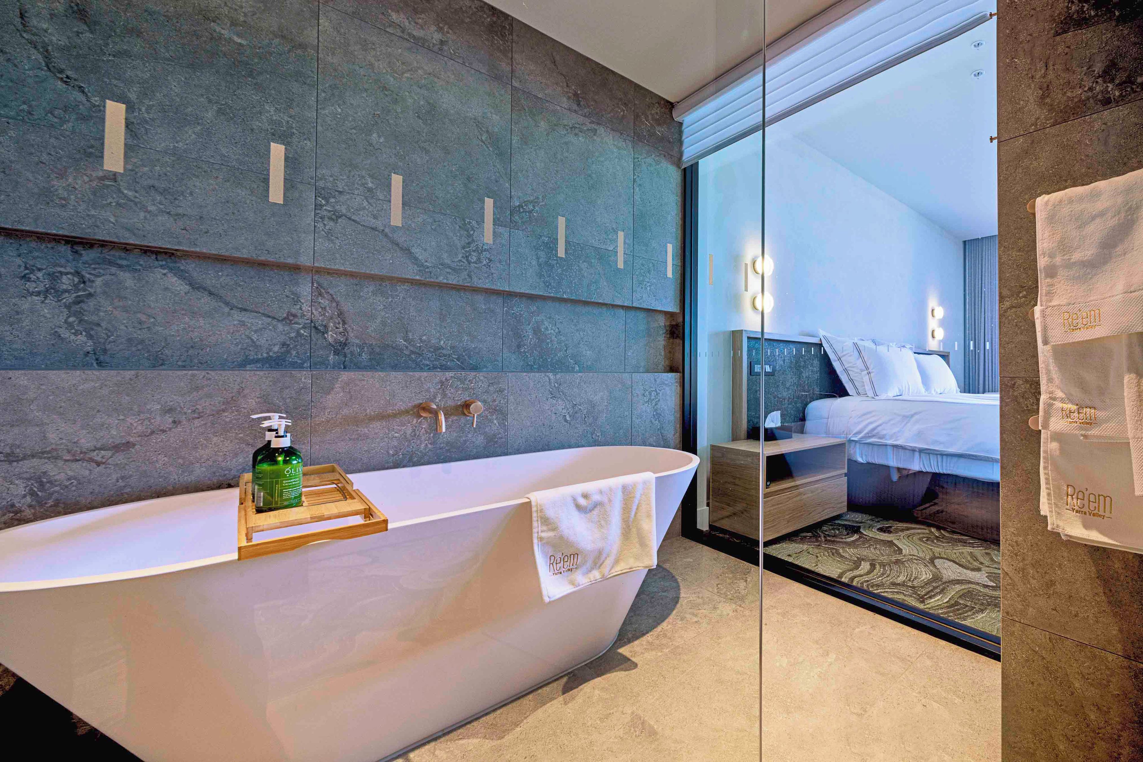 A modern bathroom with a freestanding bathtub, a wooden tray with a bottle, and a towel hanging on the side.