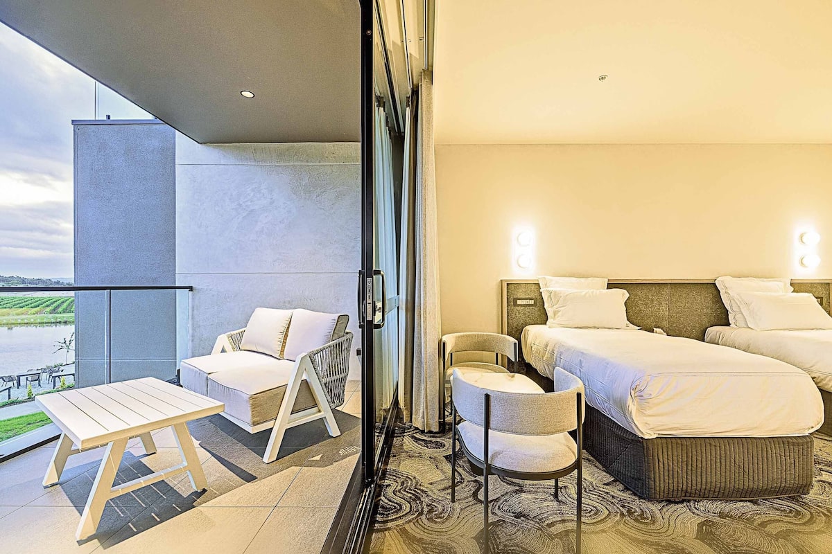 A hotel room with a balcony, a bed, a chair, and a small table.