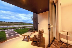 A modern outdoor patio with a table and chairs, a glass door leading to a room, and a view of a lake and fields. - Re'em Yarra Valley (Melbourne)