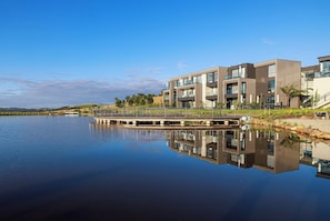 A modern building with a reflection in calm water, a bridge, and a clear sky.