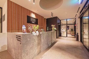 A reception desk with a wooden panel wall, a digital screen, and a sign for 'Réem'. There are white flowers on the desk, and a sign indicating private dining, meeting room, and barrel hall.