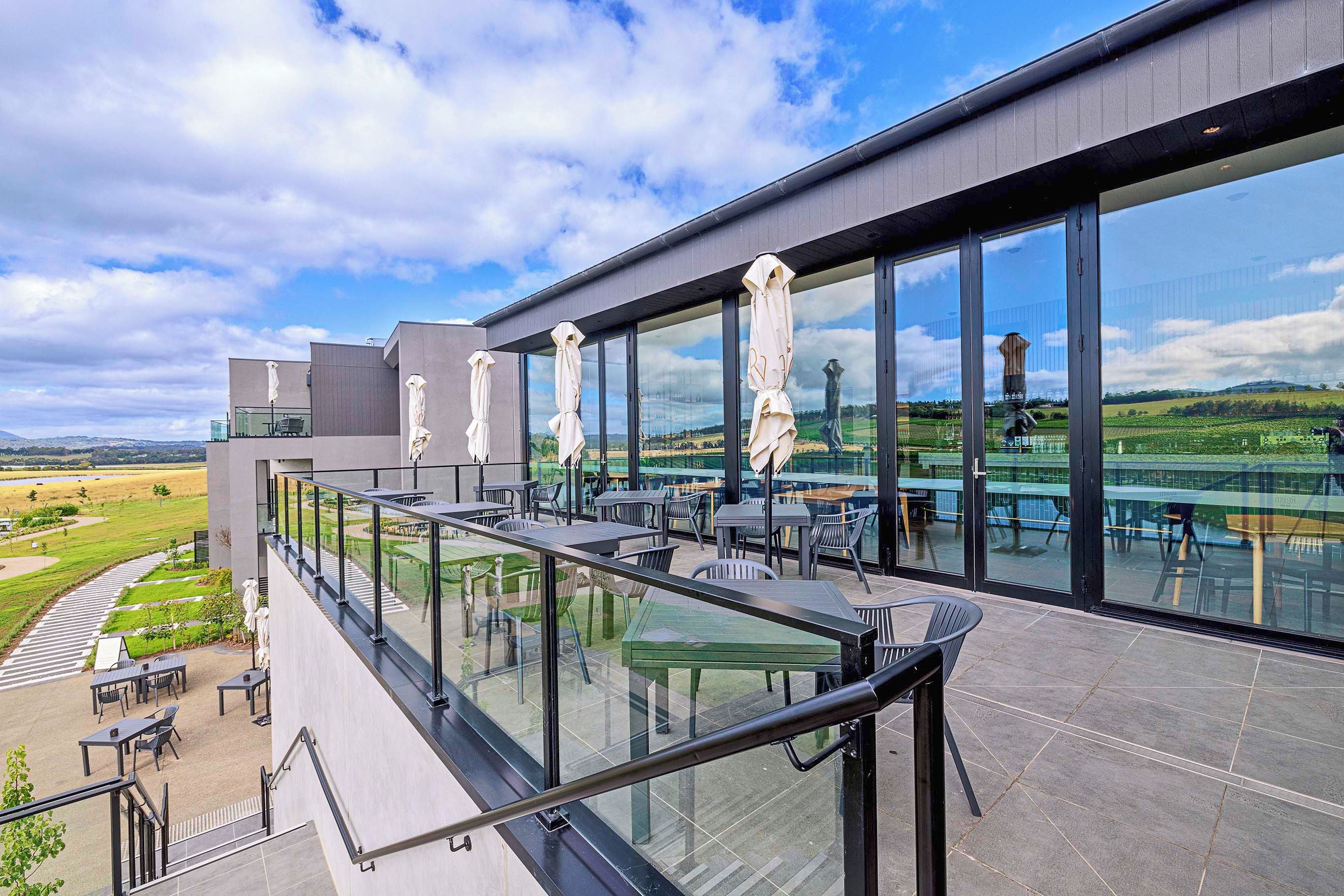 A modern outdoor terrace with glass railings, outdoor seating, and a view of a vineyard.