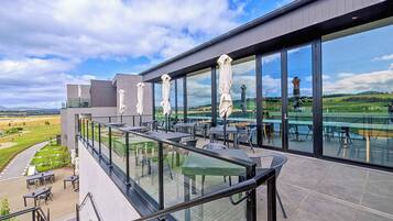 A modern outdoor terrace with glass railings, outdoor seating, and a view of a vineyard.