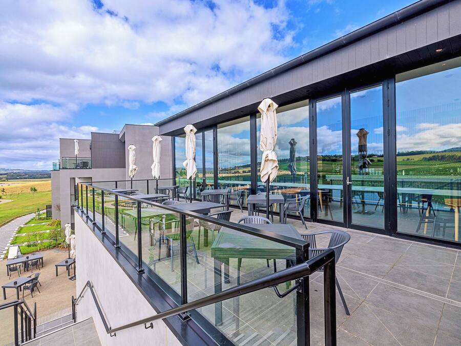 Una terraza moderna al aire libre con barandillas de vidrio, asientos exteriores y vistas a un viñedo.