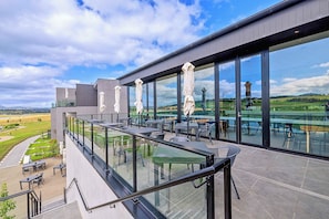 A modern outdoor terrace with glass railings, outdoor seating, and a view of a vineyard.