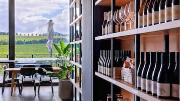 A restaurant with outdoor seating overlooking a vineyard, wine bottles on shelves, and a potted plant.