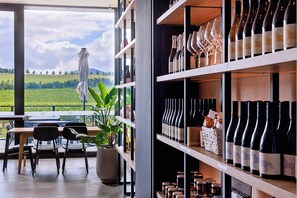 A restaurant with outdoor seating overlooking a vineyard, wine bottles on shelves, and a potted plant. - Re'em Yarra Valley (Melbourne)
