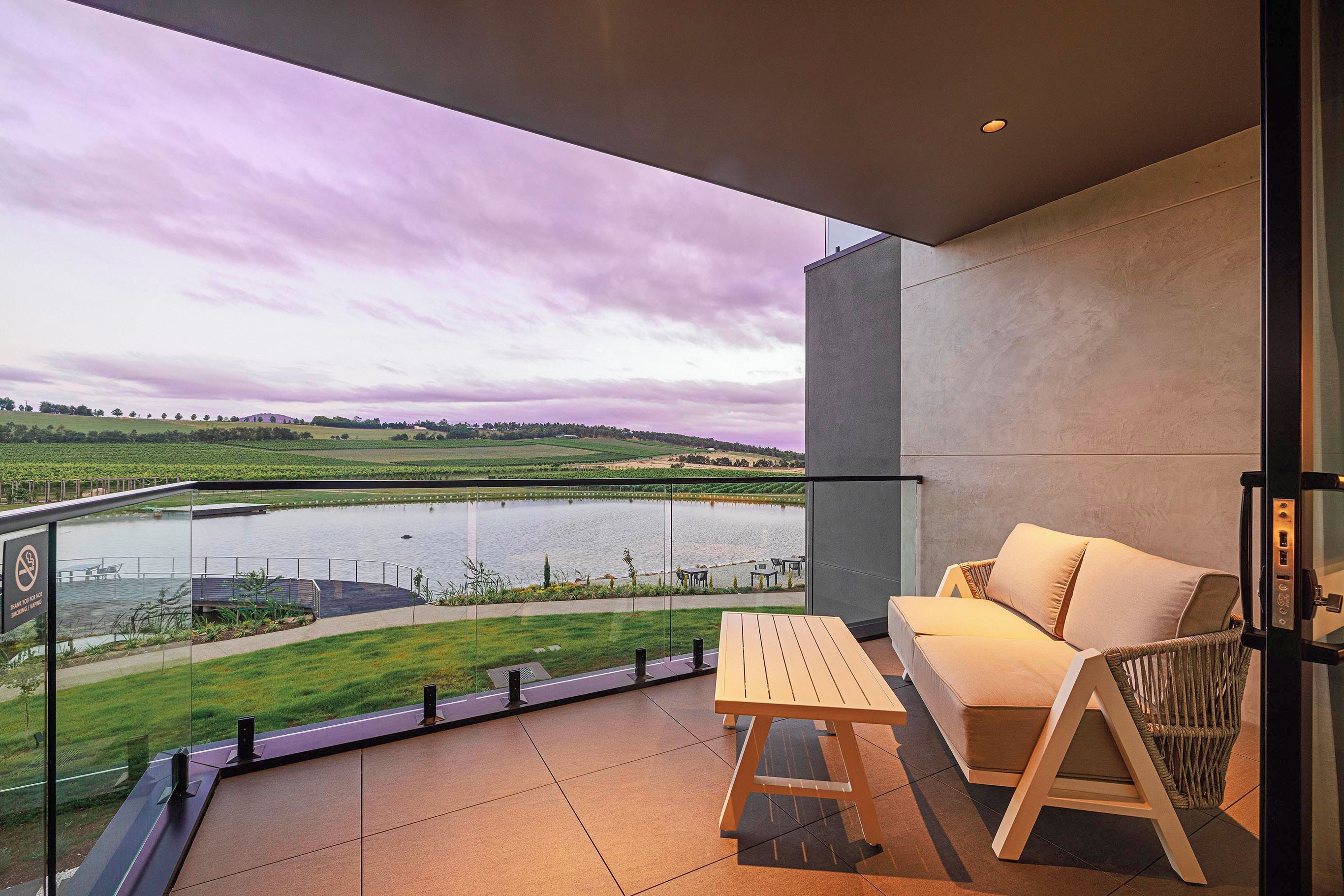 A balcony with a view of a lake, a wooden table, and a sofa.