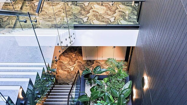 Un escalier moderne avec des rampes en verre, entouré d’une végétation luxuriante et agrémenté de motifs décoratifs sur les murs.