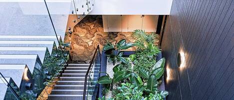 Una escalera moderna con barandillas de vidrio, rodeada de abundante follaje y diseños de pared con motivos.