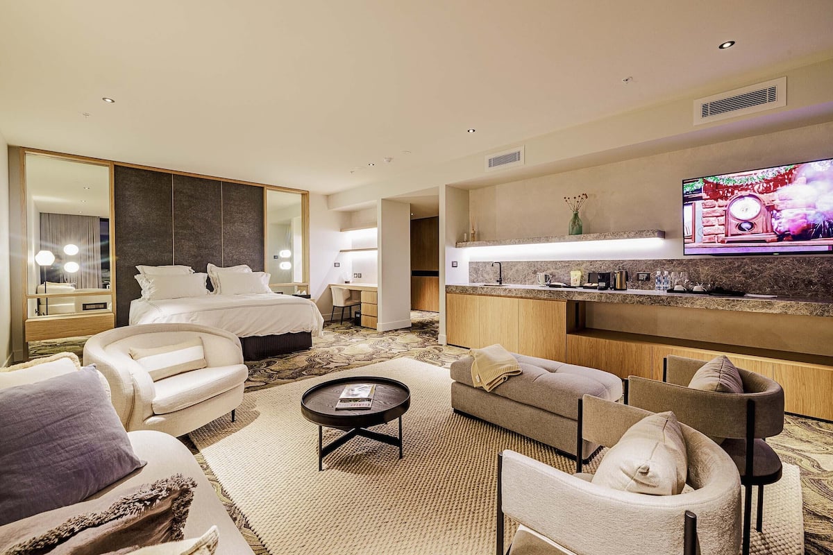 A hotel room with a bed, a sofa, a coffee table, a TV, and a kitchen area.