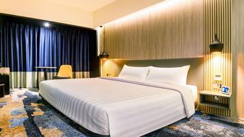 A hotel room with a large bed, a desk, a chair, and a nightstand with a lamp.