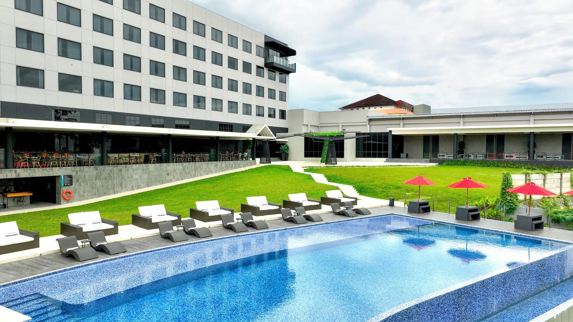 Un hotel con piscina, mobiliario exterior y césped cuidado.