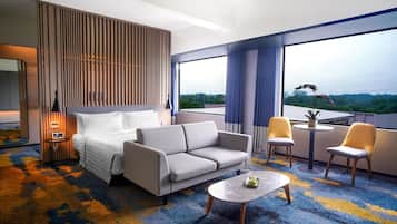 Habitación de hotel con cama, sofá, una mesita y balcón con sillas.
