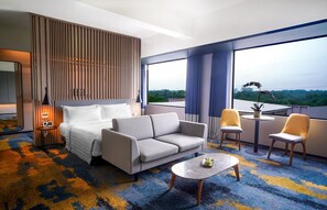 A hotel room with a bed, a sofa, a small table, and a balcony with chairs. - Aston Serang Hotel & Convention Center (Serang)