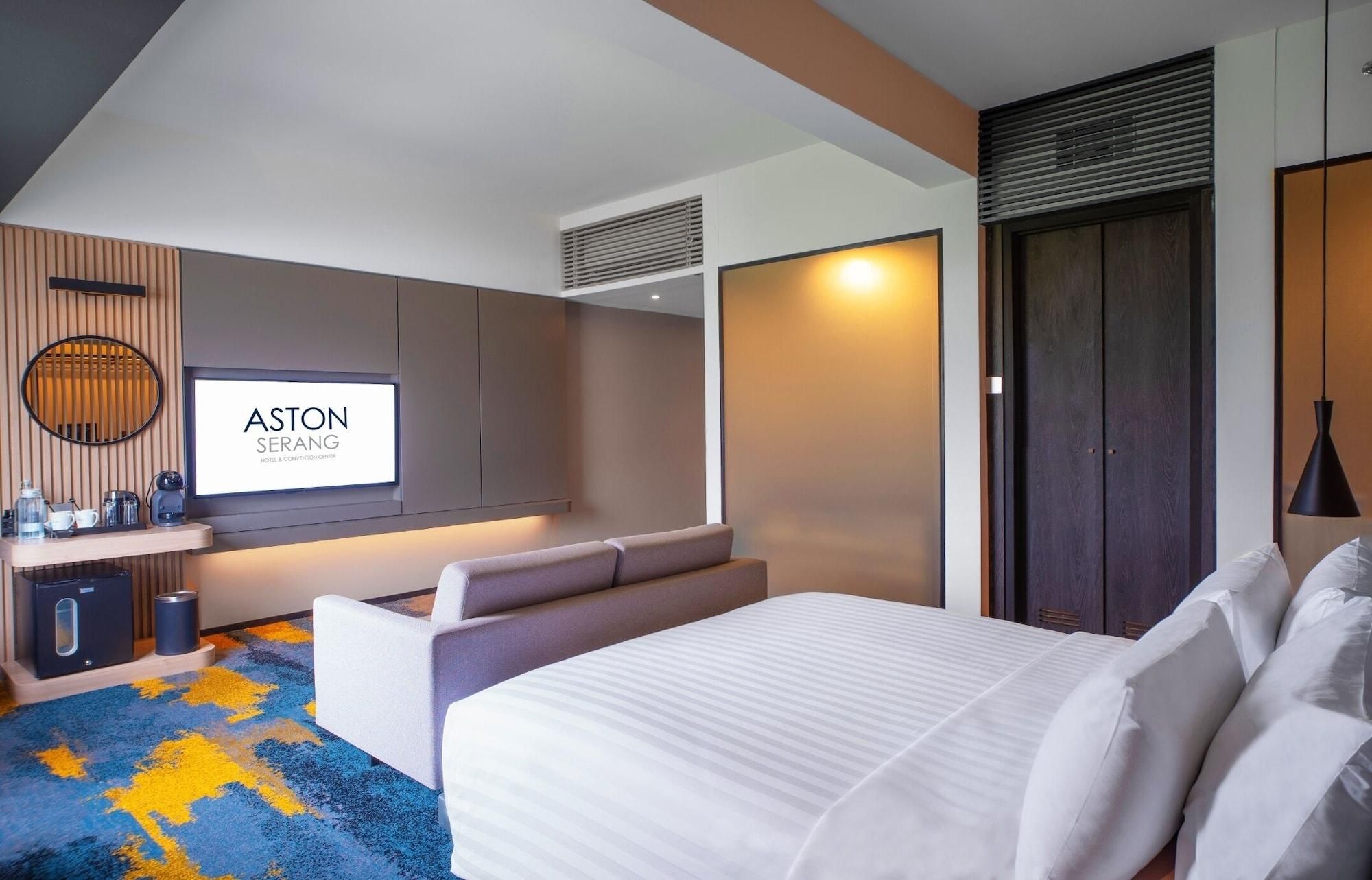 A modern hotel room with a large bed, a seating area, a television, and a minibar.