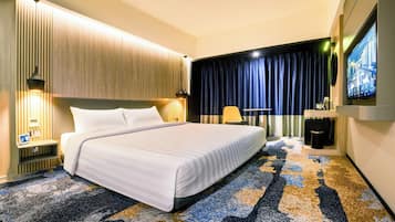 A hotel room with a large bed, a desk with a chair, a coffee machine, and a TV on the wall.