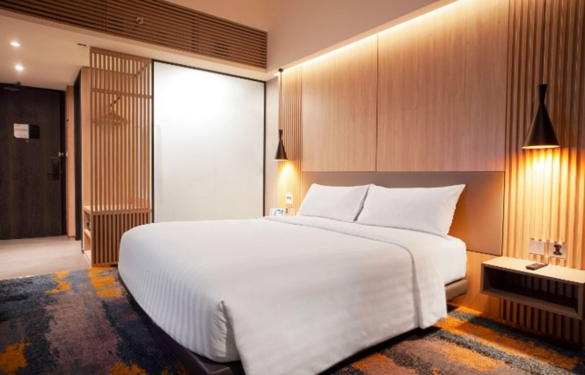 A modern hotel room with a large bed, wooden paneling, and a nightstand with a lamp.