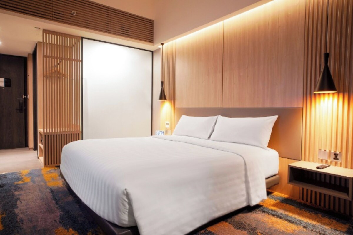 Ein modernes Hotelzimmer mit einem großen Bett, Wandverkleidung aus Holz und einem Nachttisch mit einer Lampe.