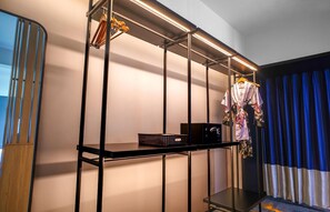 A hotel room with a black metal shelf unit, a small table, and a blue curtain. - Aston Serang Hotel & Convention Center (Serang)