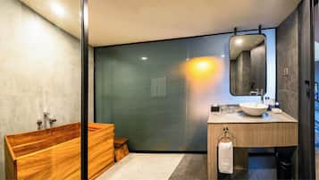 A modern bathroom with a wooden bathtub, a large mirror, and a sink with a towel ring.