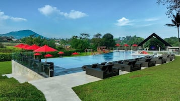 A swimming pool with red umbrellas, lounge chairs, and a glass balustrade.