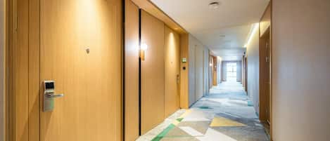 A hotel hallway with wooden doors, a patterned carpet, and a bright light at the end.