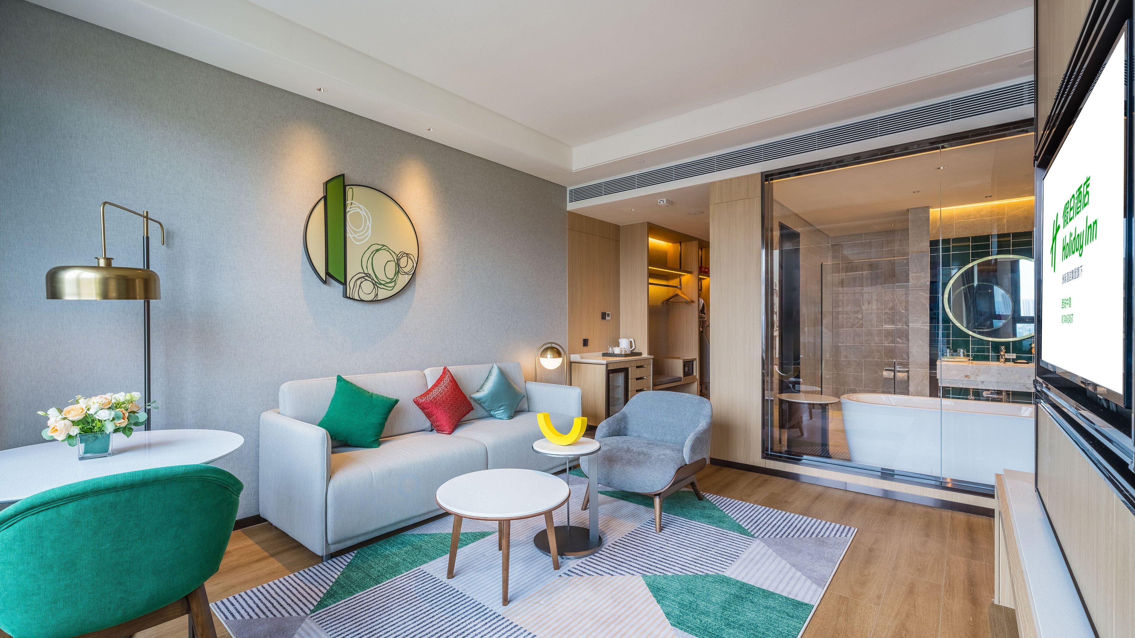 A modern hotel room with a sofa, armchairs, a small table, and a glass shower area.