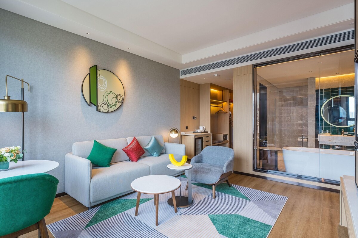 A modern hotel room with a sofa, armchairs, a small table, and a glass shower area.