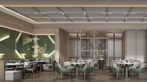 A modern dining area with round tables and green chairs, featuring a geometric wall design and recessed lighting. - Holiday Inn Xian East (Xi'an)