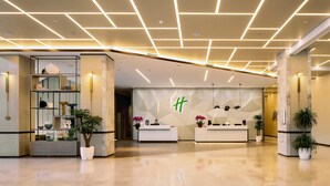 A modern hotel lobby with a reception desk, geometric wall design, and potted plants. - Holiday Inn Xian East (Xi'an)