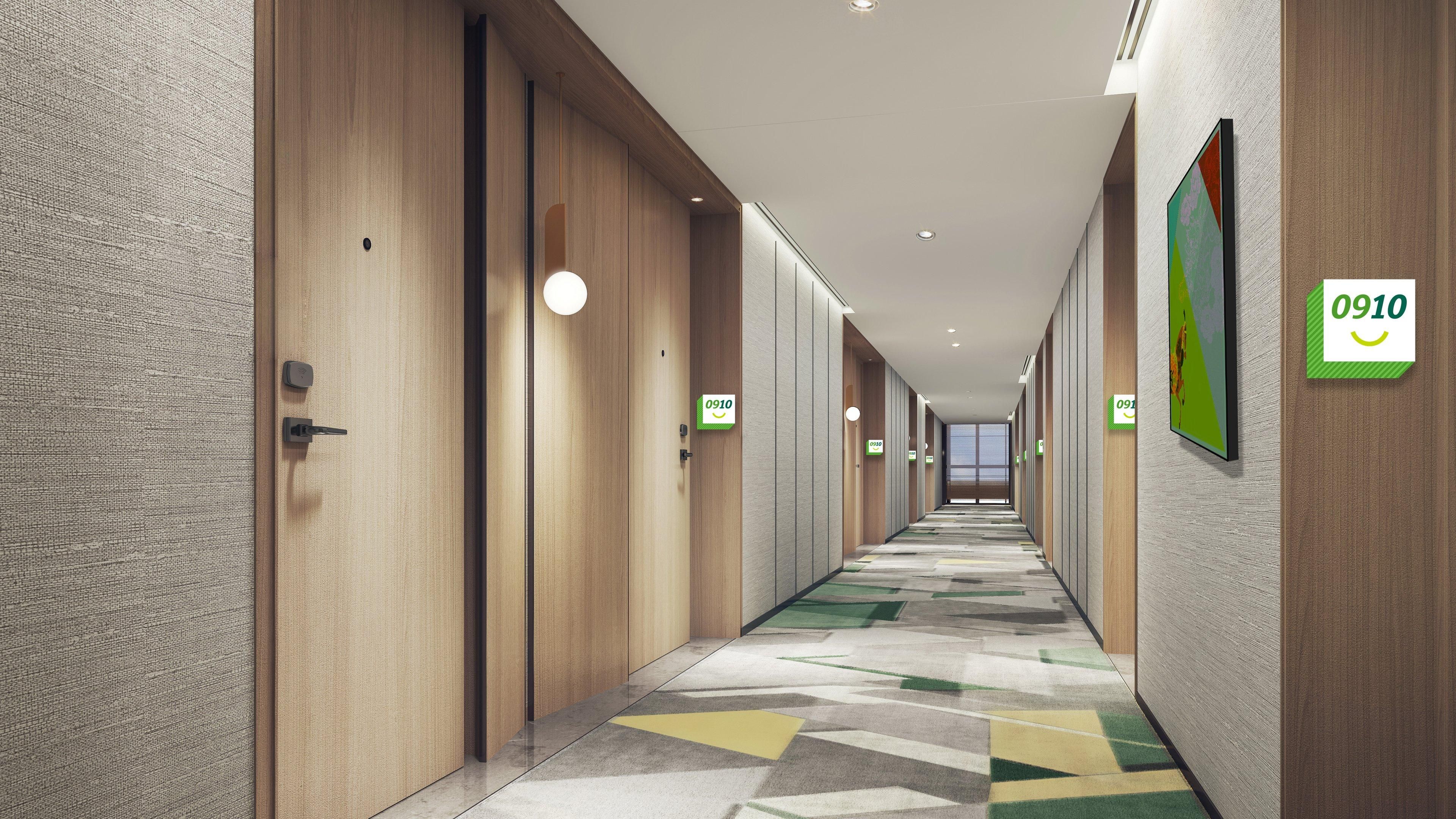 Un corridoio moderno di un hotel con porte in legno, targhette numerate per le camere e un tappeto a motivi decorativi.