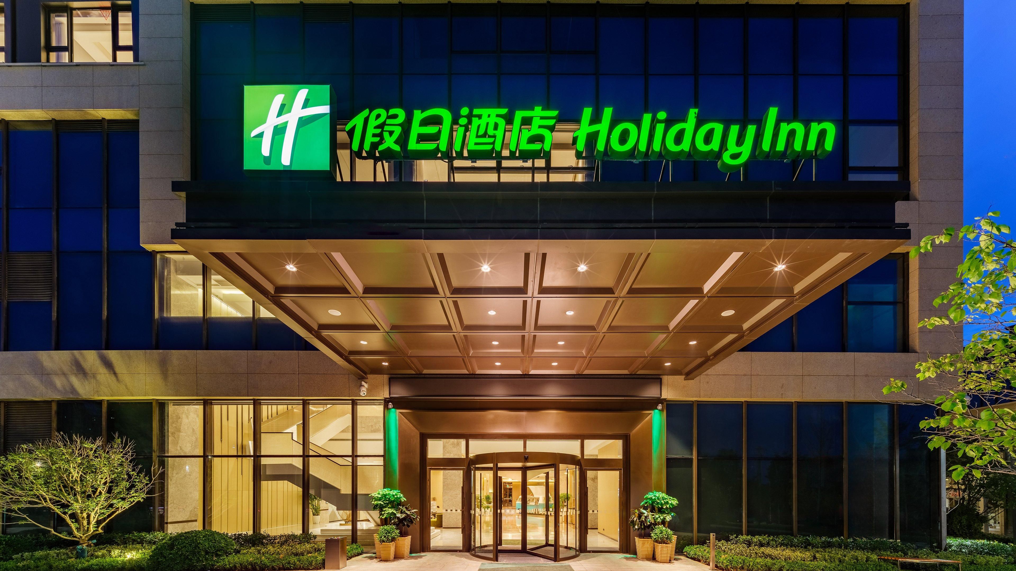 De ingang van een Holiday Inn hotel met een modern ontwerp, met een glazen gevel en een draaideur.